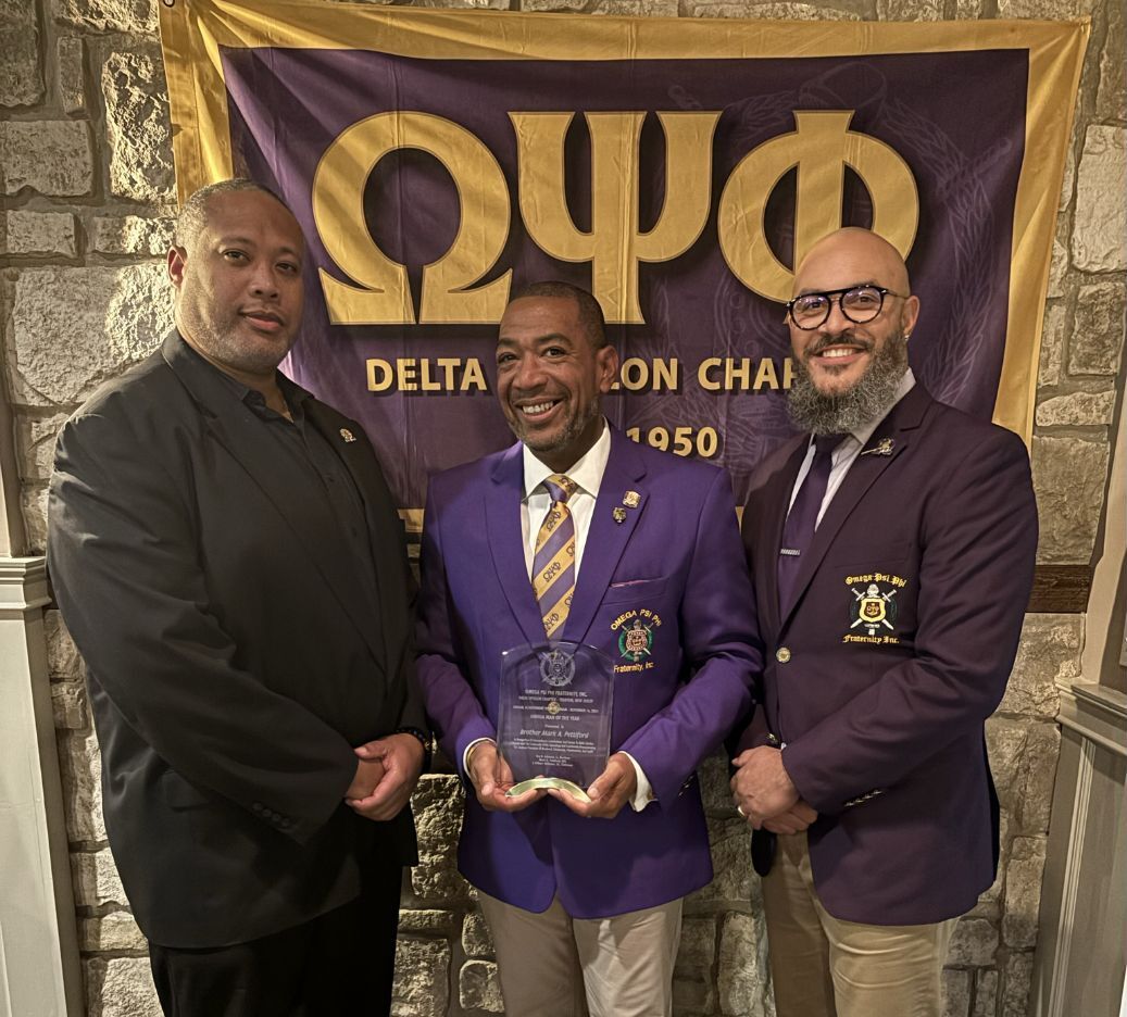 Mark Pettiford centered between two brothers while holding his plaque